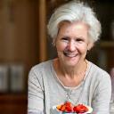 Eine elegante, alterslose Frau lächelt sanft und hält eine Schale mit frischen Früchten, die jugendliche Vitalität und Anti-Aging-Ernährung symbolisiert.